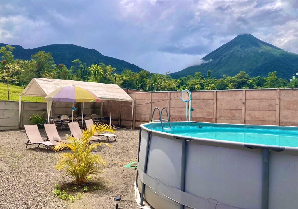 cenic outdoor area at a Tropical Glow rental property in La Fortuna, Costa Rica, featuring a swimming pool with panoramic views of Arenal Volcano and lush surroundings.