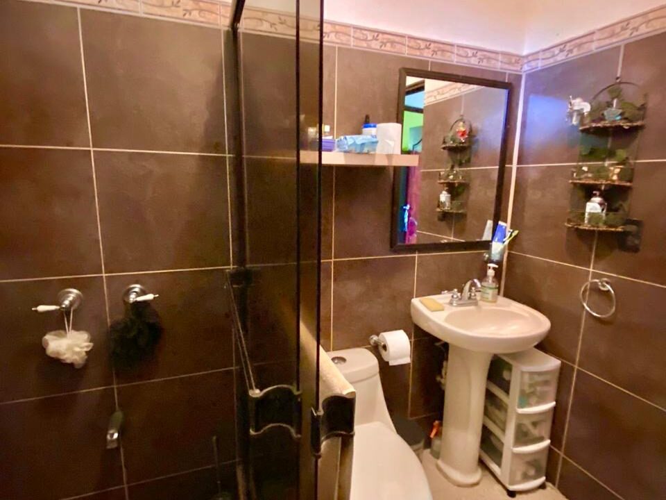 Shower bathroom with stone flooring and storage shelves – La Fortuna Costa Rica Real Estate  Earth-toned bathroom with river-stone shower floor and built-in shelving in a tranquil property for sale in La Fortuna Costa Rica. Tropical Glow.