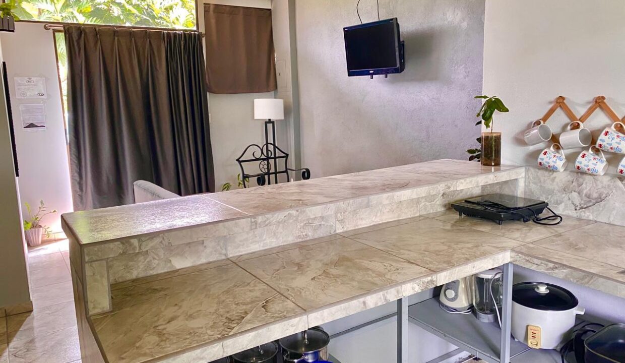 Open kitchen with tiled counter and wall-mounted TV in La Fortuna Airbnb apartment