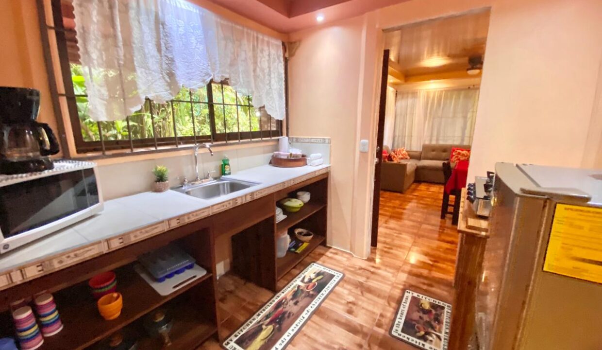 Functional and welcoming kitchen layout with open storage, dual sink, and tile countertops